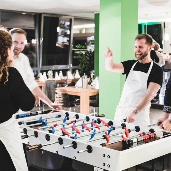 Kickertime statt Kaffeepause – Teilnehmer während der Tischkicker-Challenge beim Teamworkshop im Kochatelier Köln. Kickertime statt Kaffeepause – Teilnehmer während der Tischkicker-Challenge beim Teamworkshop im Kochatelier Köln.